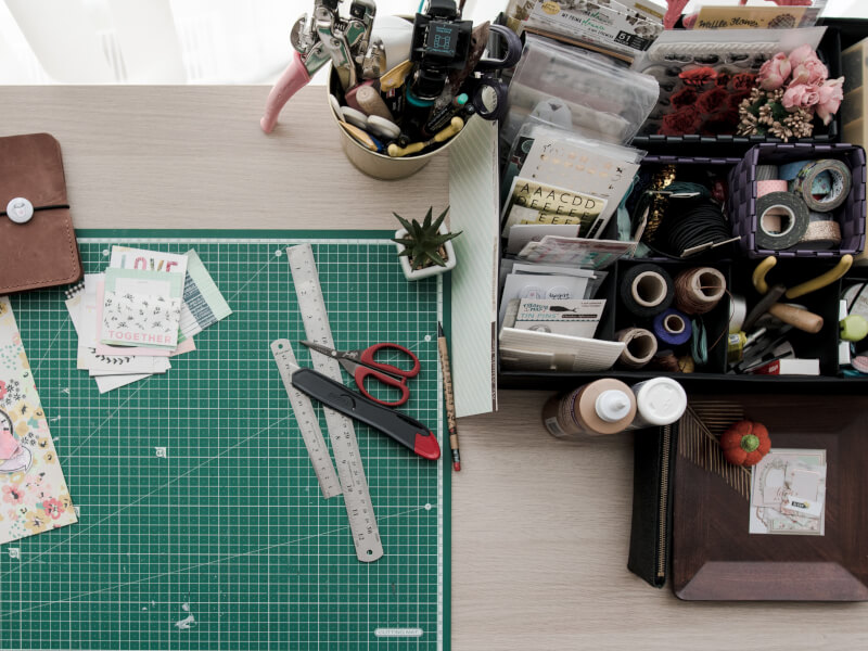 A table scattered with crafting tools and paper including a cutting mat